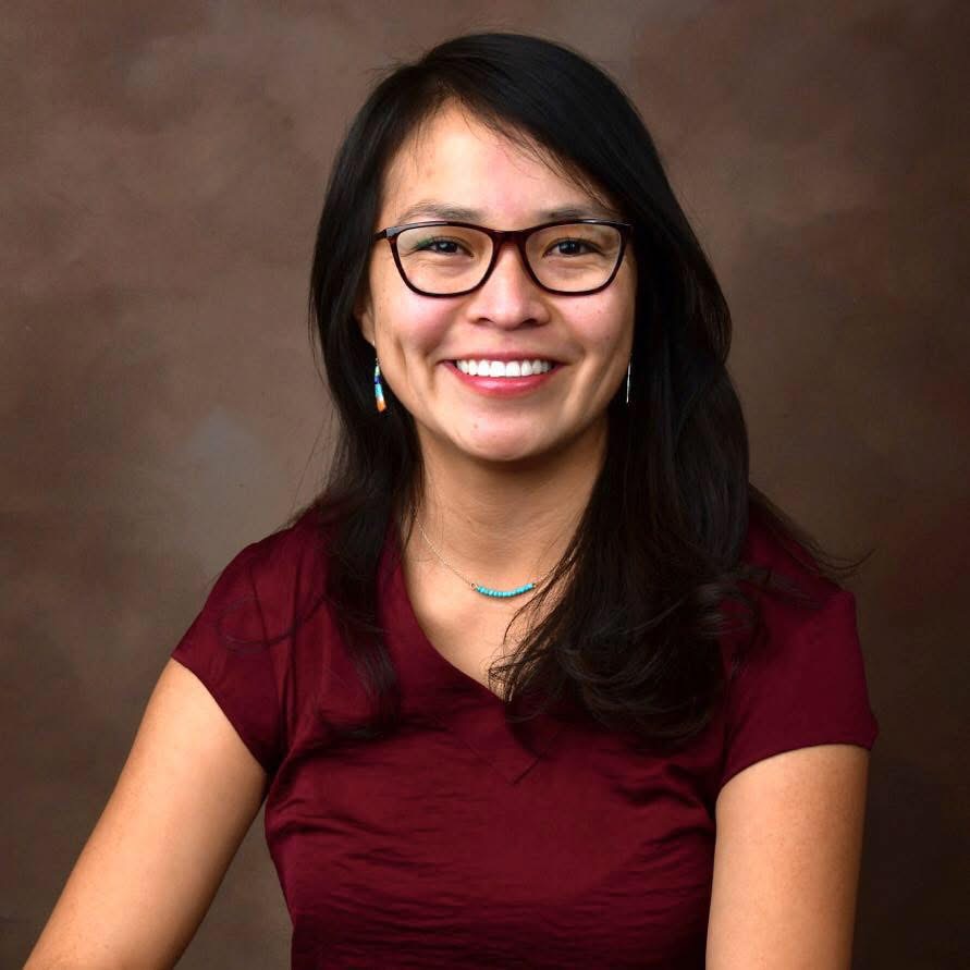 Smiling woman with glasses in a maroon top against a brown studio background.